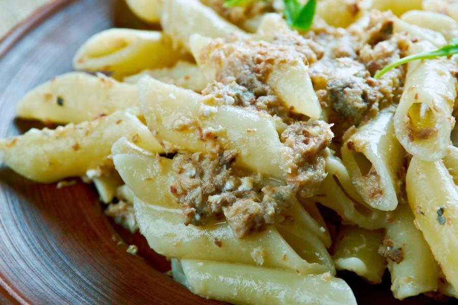 Pasta corta con sardinas desmenuzadas y salsa de aceite de oliva, servida en un plato marrón y decorada con hojas verdes.