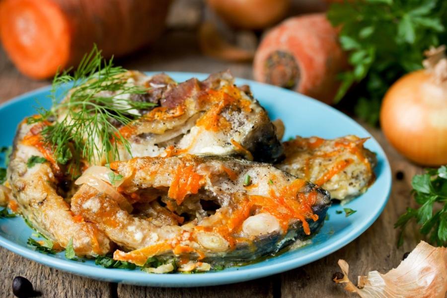 Rodajas de pescado en escabeche con zanahoria y cebolla, servidas en un plato azul y decoradas con eneldo fresco.