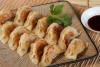 Una fuente con gyoza ya cocinado y un cuenco con salsa para mojar al lado.