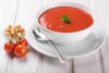 Sopa de tomate en una taza de loza blanca sobre una mesa de madera blanca.