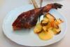 Un plato con una pierna de cochinillo asado acompañada de patatas. 
