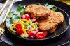Dos chuletas sin palo de cordero empanado con ensalada de tomate.
