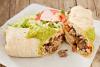 Burrito de carne servido con guacamole por encima y acompañado con ensalada.