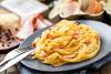 Un plato de cintas a la carbonara con algunos de los ingredientes al fondo.