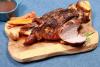 Una pierna de cordero asada sobre una tabla de madera con zanahorias, patatas y romero, 