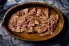 Cuatro filetes de hígado encebollado en una fuente de barro.