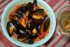 Mejillones con tomate en un plato hondo con una copa de vino blanco al lado.