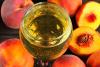 Una copa de vino blanco, vino de melocotón, rodeada de melocotones.