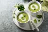 Dos tazas con porciones individuales de sopa de guisantes decorada con nata líquida y menta.