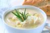 Una taza con sopa de coliflor decorada con romero y queso rallado.