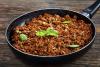 Una sartén con esta receta de carne picada guisada decorada con hierbas frescas.