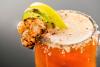 Un vaso de michelada escarchado con sal y decorado con colas de camarones, una rodaja de lima y una rodaja de limón.