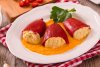 Un plato con tres pimientos del piquillo rellenos de pescado rodeados con la salsa.