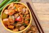 Un cuenco con pollo kung pao. Hay dos palillos al lado.