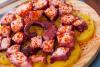 Pulpo a la gallega acompañado de rodajas de patata cocida en plato de madera.