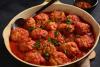 Una cazuela de cerámica con albóndigas de sepia y gambas en salsa de tomate.