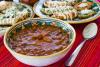Un plato hondo con frijoles charros y otros con tacos dorados y sopes al fondo.
