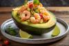 Aguacate relleno de cebiche de gambas sobre un plato, acompañado con trozos de lima.
