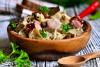 Bigos tradicional polaco servido en un cuenco rústico de madera sobre una mesa de madera desgastada, con chucrut, trozos de cerdo, rodajas de salchicha, champiñones y adornado con perejil fresco.