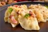 Plato con tres pierogies cubiertos con cebolla salteada y tocino, servido con chucrut.