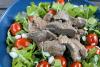 Una ensaladera baja con ensalada de carne al estilo vietnamita hecha con filetes de cadera y hojas variadas.
