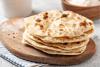 Una pila de panes planos tipo chapati recién hechos, colocados sobre una tabla de madera con un paño rayado debajo.