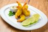 Gambas con gabardina elegantemente apiladas en un plato, acompañadas con mayonesa y rodajas de limón, deocradas con unas hojas de perejil..