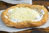 Lángos con nata agria y queso rallado sobre una measa de madera.