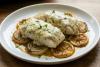 Dos filetes de pescado al horno con salsa cremosa de hierbas; imagen sintética.