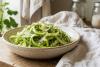 Una ensalada casera de espárragos laminados, con finas cintas de espárragos verdes frescos y crudos, apilados de forma natural en un tazón rústico de cerámica, adornados con delicado queso parmesano rallado y ralladura de limón