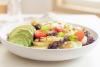 Plato de ensalada con aguacate en láminas, tomates cherry, hojas verdes y piñones; imagen sintética.