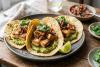 Tres tacos de maíz con cubos de queso a la plancha, aguacate machacado, pico de gallo, cilantro y una cuña de lima.