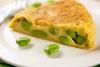 Porción de tortilla española con habas tiernas en un plato blanco.