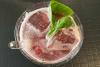 Un vaso con limonada de frambuesa e hibisco alemana, con hielo y hojas de albahaca.