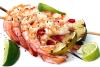 Brochetas de gambas a la parrilla con rodajas de lima asada, gajos de lima fresca y chile rojo sobre un plato blanco.