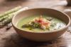 Cuenco de gazpacho verde de espárragos trigueros decorado con huevo cocido, puntas de espárrago, jamón serrano y aceite de oliva sobre una mesa rústica.