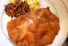 Schnitzel dorado con sal en escamas, acompañado de ensalada de patata y setas salteadas en un plato blanco.