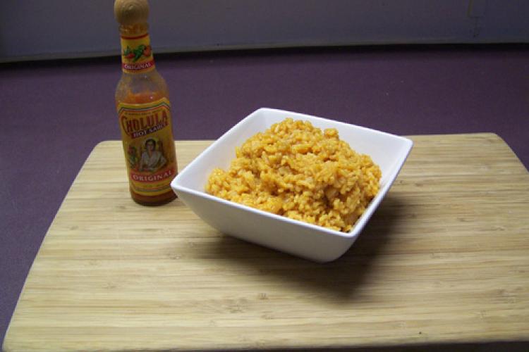 Un recipiento con arroz al estilo mexicano sobre una mesa con una botella de salsa al lado.