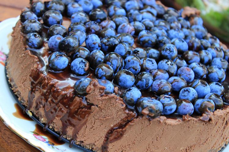 Tarta de queso con chocolate y café decorada con jarabe de chocolate y arándanos azules.