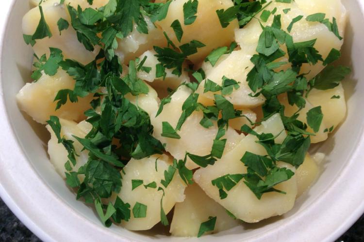 Detalle de patatas hervidas con mantequilla y perejil en una cazuela de loza blanca.