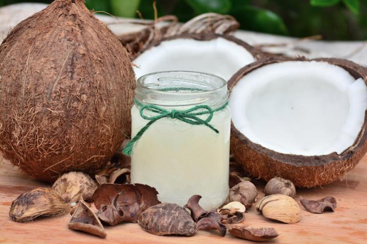 Cocos junto a un recipiente de vidrio con aceite de coco.