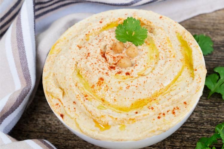 Hummus casero en un cuenco decorado con garbanzos cilantro, grabanzos cocidos y aceite de oliva.
