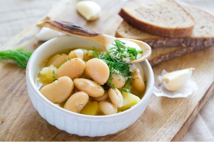 Un cuenco con sopa de alubias blancas con patata, hierbas frescas y nata agria.