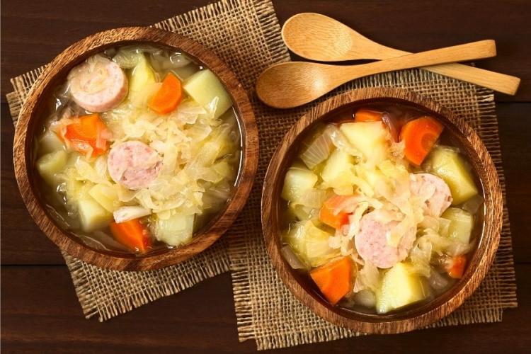 Sopa de salchichas con chucrut, zanahorias y patatas en cuencos de loza.