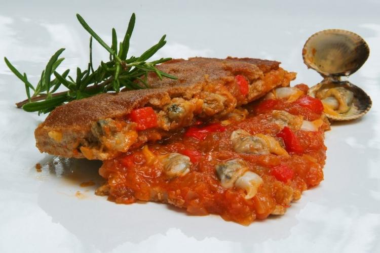 Un trozo de empanada gallega con rellendo de berberechos, pimiento asado y salsa de tomate.
