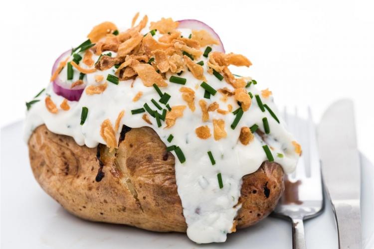Una patata asada cubierta con nata agria, cebollino y cebolla crujiente.