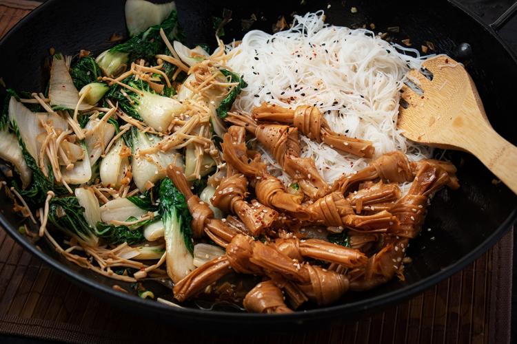 Bok choi salteado con enokis y nudos de tofu servido con fideos finos de arroz.