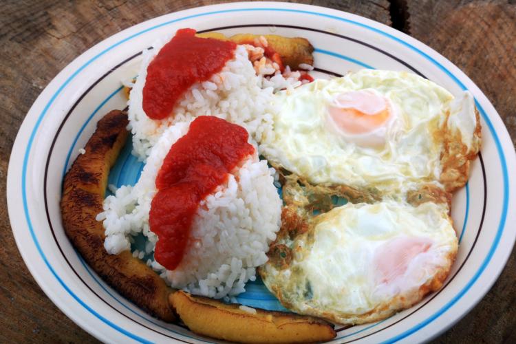 Un plato de arroz a la cubana con arroz blanco, salsa de tomate, huevos fritos y plátano frito.
