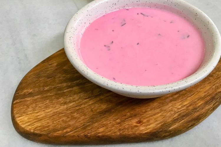 Un cuenco de loza blanca lleno de sopa de remolacha y yogur situado sobre una tabla de madera.
