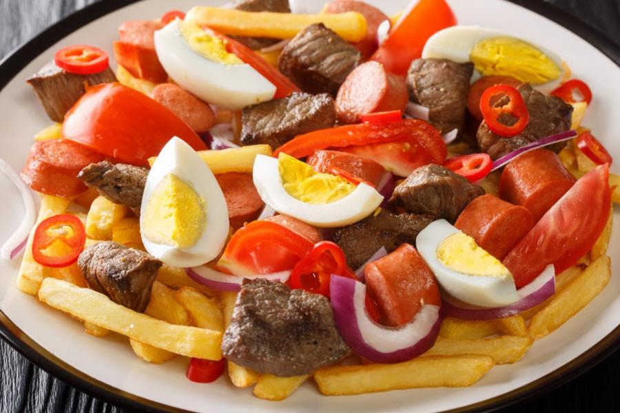 Un plato de pique a lo macho con carne mixta, salchichas, papas fritas, huevos duros, tomates, cebollas y chiles.